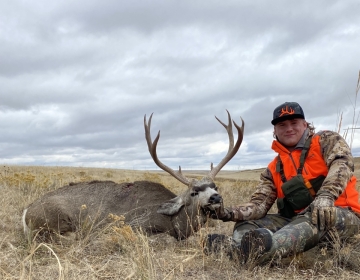 Hunter posing with his mule deer under a cloudy sky